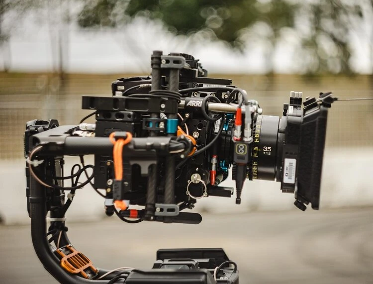 Professional ARRI cinema camera with a prime lens is mounted on a rig in a studio or on location, with an overcast sky in the background.
