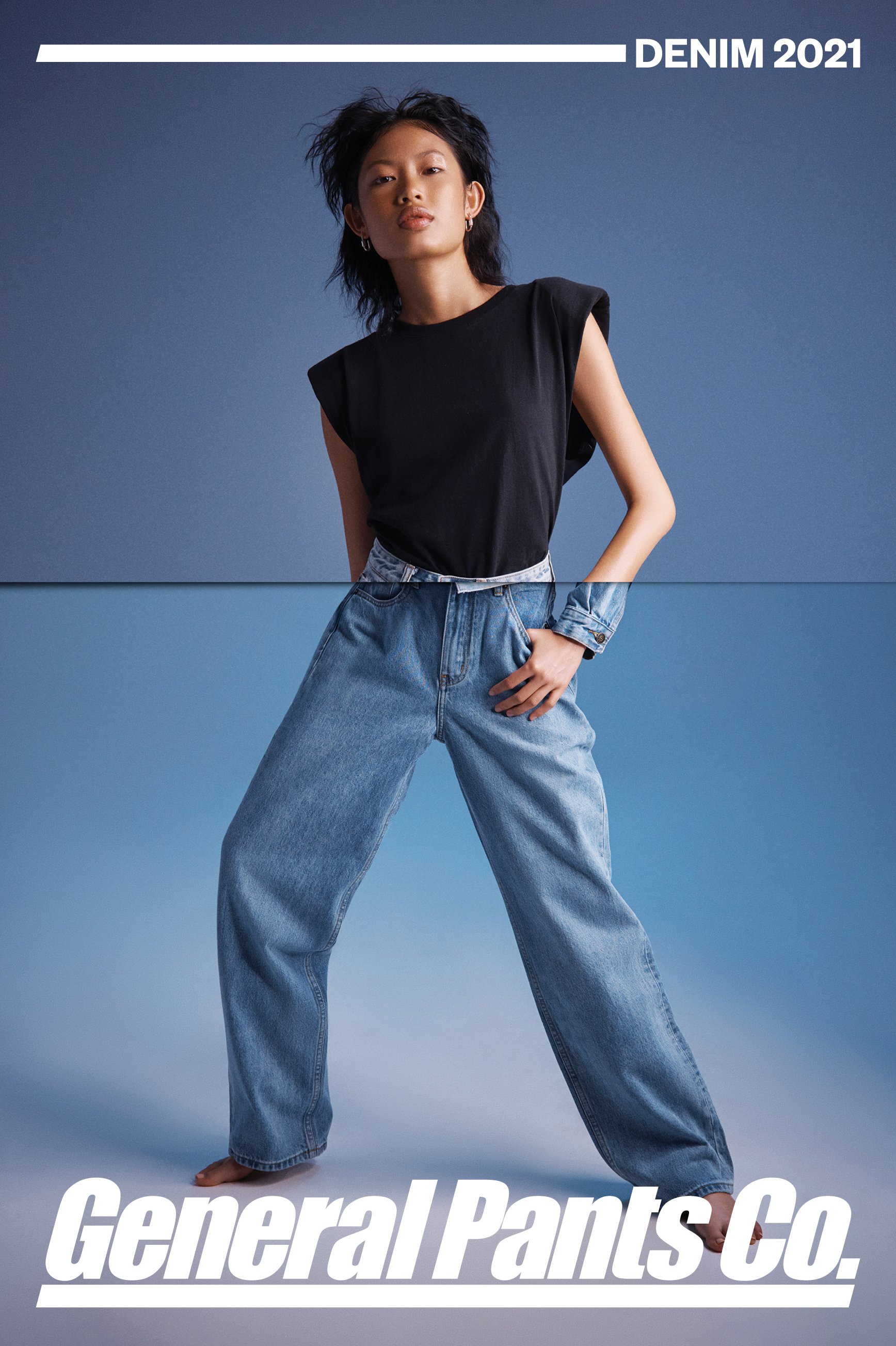 Fashion shot of an Asian female model in denim pants and a black top, posing against a graduated blue background in a studio setting.