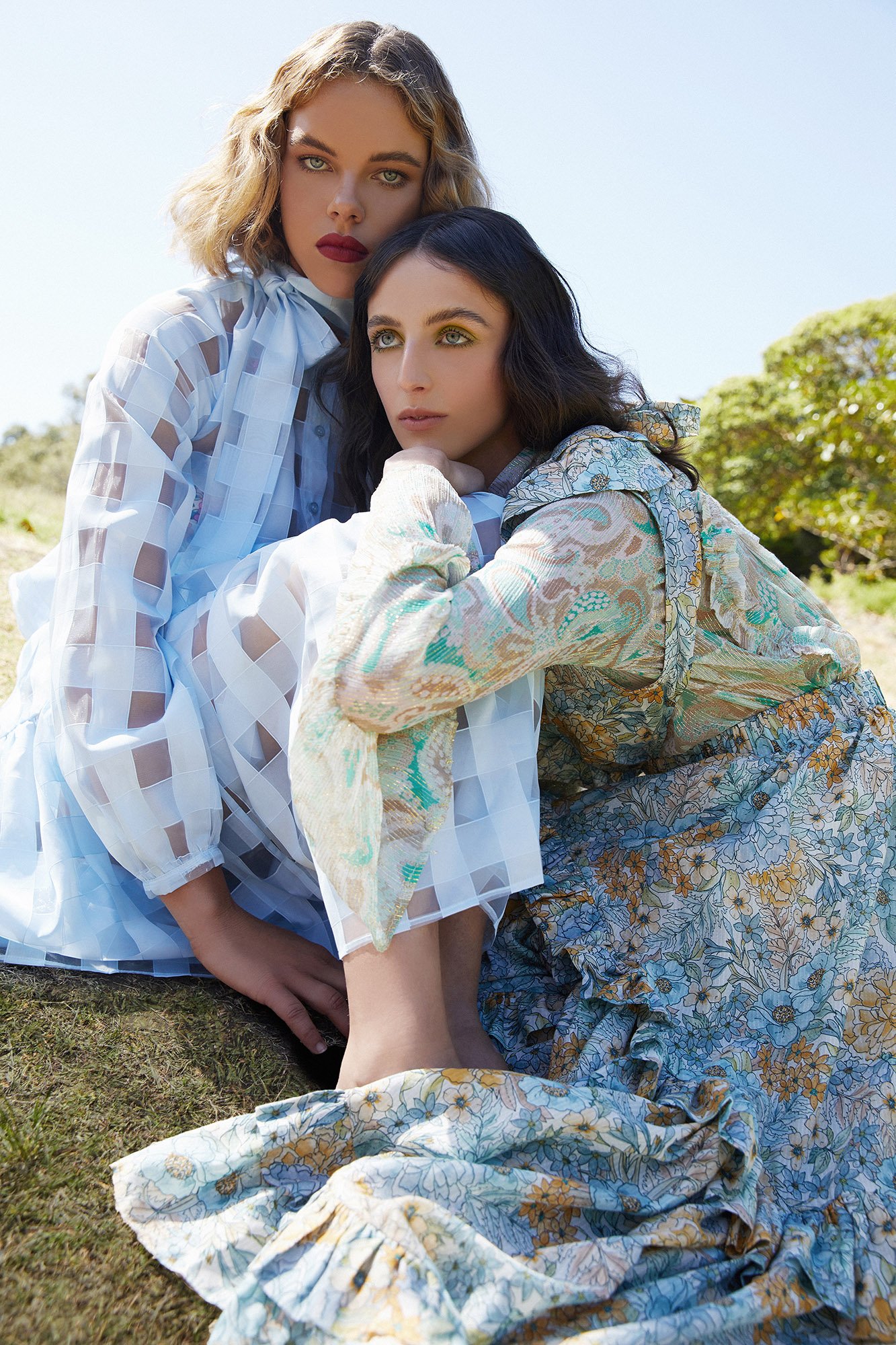 Two female models in patterned blue dresses posed outdoors on grass styled by Emma Cotterill