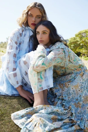 Two female models in patterned blue dresses posed outdoors on grass styled by Emma Cotterill