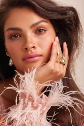 Close-up portrait of a woman with dark hair wearing feather-cuff sleeve, pearl earrings, and gold rings, styled by Emma Cotterill.