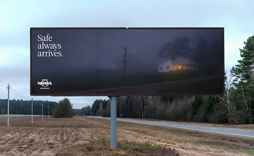 Billboard showcasing a house amidst fog at dusk, promoting NRMA Insurance with the tagline 'Safe always arrives' against a rural backdrop.