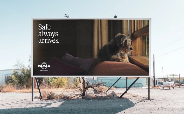Billboard displaying an ad with a dog resting on cushions and text that reads Safe always arrives by Bear Meets Eagle On Fire.