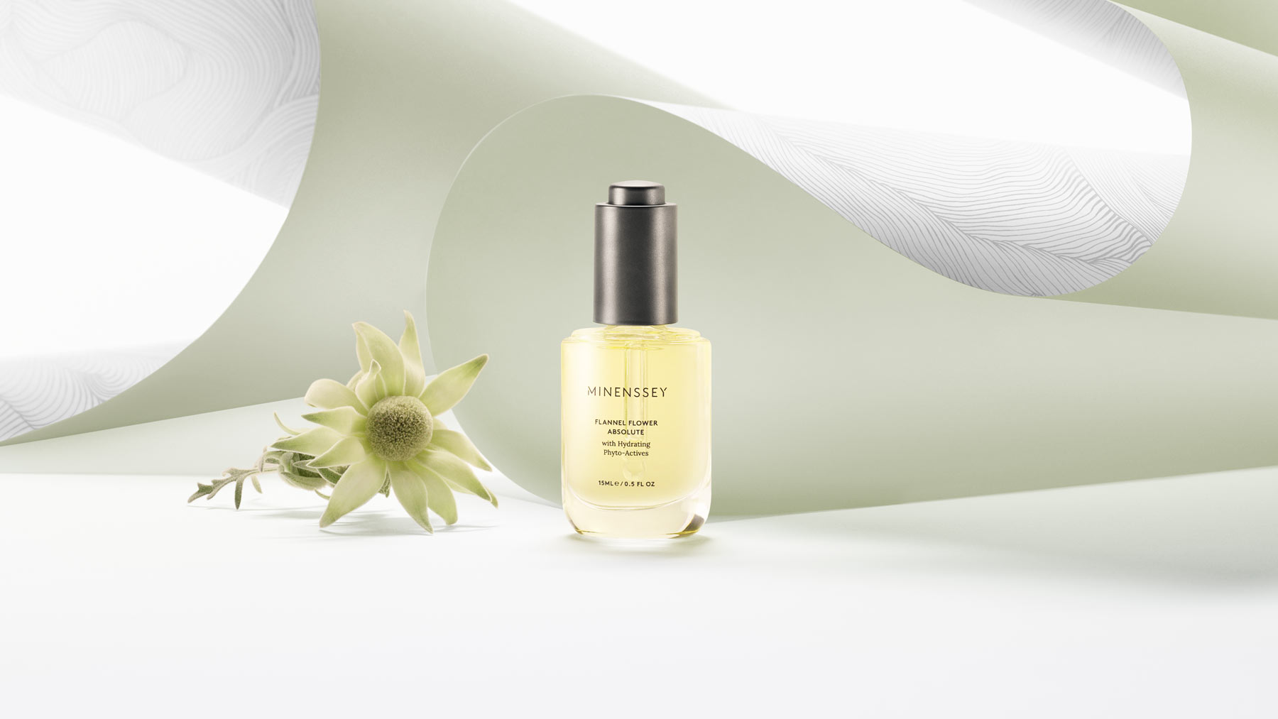 Cosmetic serum product shot: Oil bottle and flannel flower against an abstract paper background in pale green and white tones.