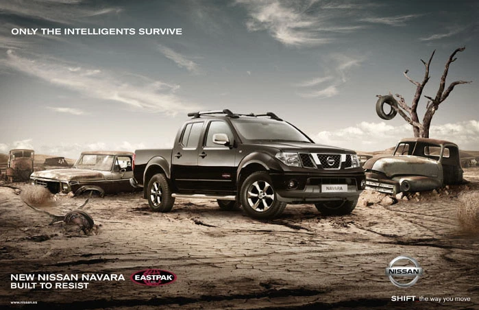 Nissan Navara pickup truck stands in a barren landscape amongst rusted, derelict vehicles under a partly cloudy sky, advertising resilience.