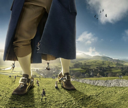 Fantasy image of a giant and miniature people on a grassy hillside beneath a blue sky. Features large legs, period shoes, and miniature humans.