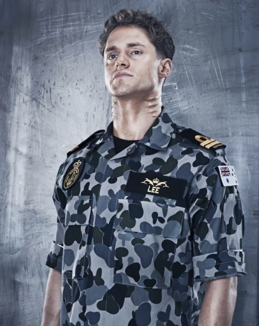 Portrait of a young adult male wearing a camouflage-patterned military uniform, looking upwards against a grey industrial background.