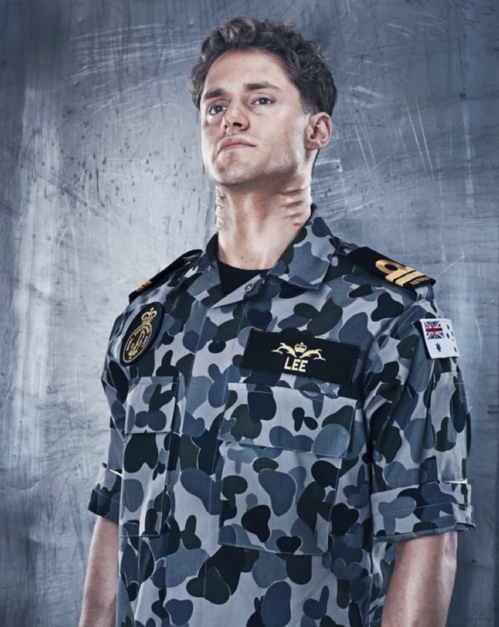 Portrait of a man in a grey camouflage military uniform with name patch against a textured wall
