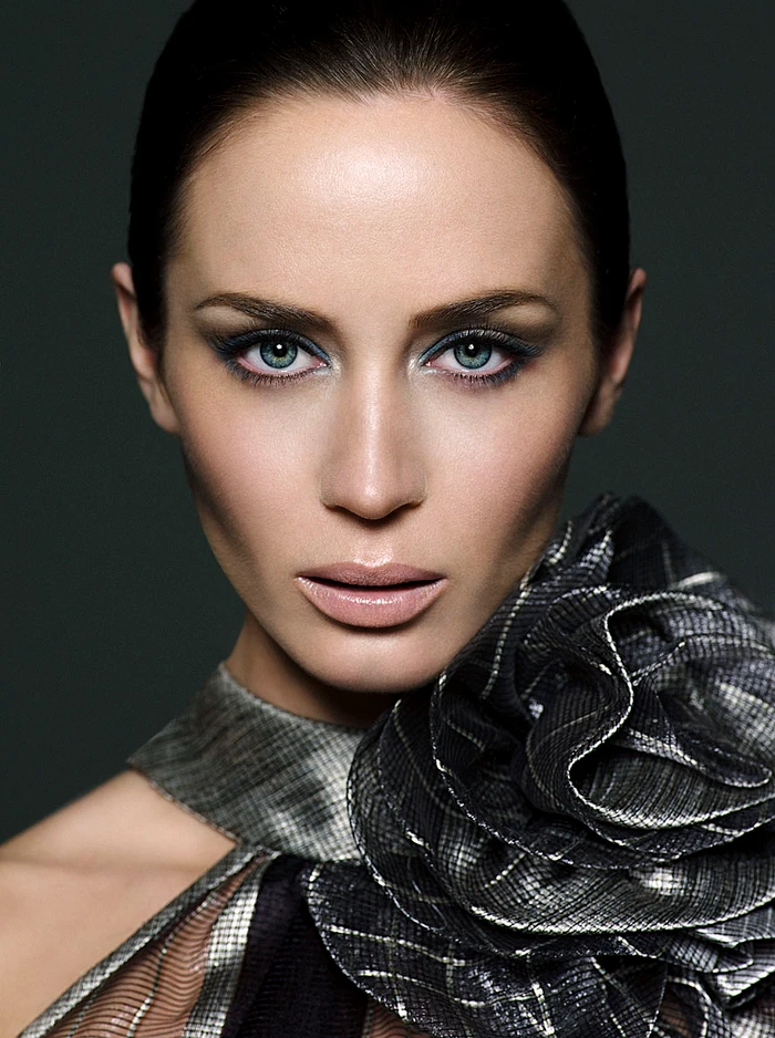 Close-up portrait of Emily Blunt wearing a textured metallic silver halter top with a large floral ruffle detail.