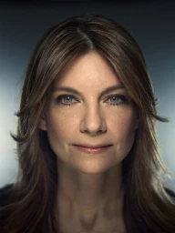 Close-up portrait of a woman with long brown hair and blue eyes, looking directly at the camera with a subtle expression.
