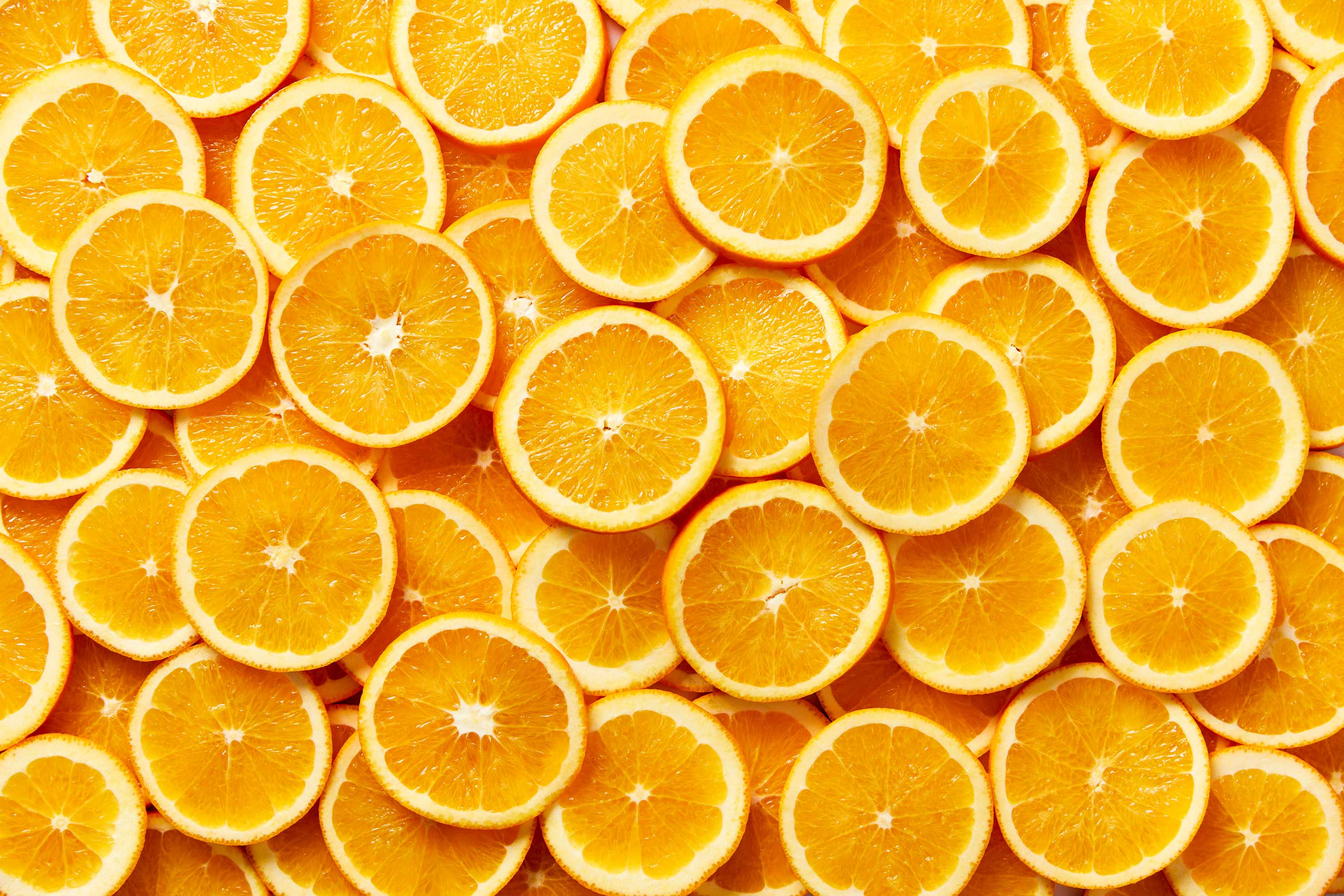 Overhead shot of vibrant orange slices arranged in a dense, textured pattern, showcasing their juicy pulp and bright color.
