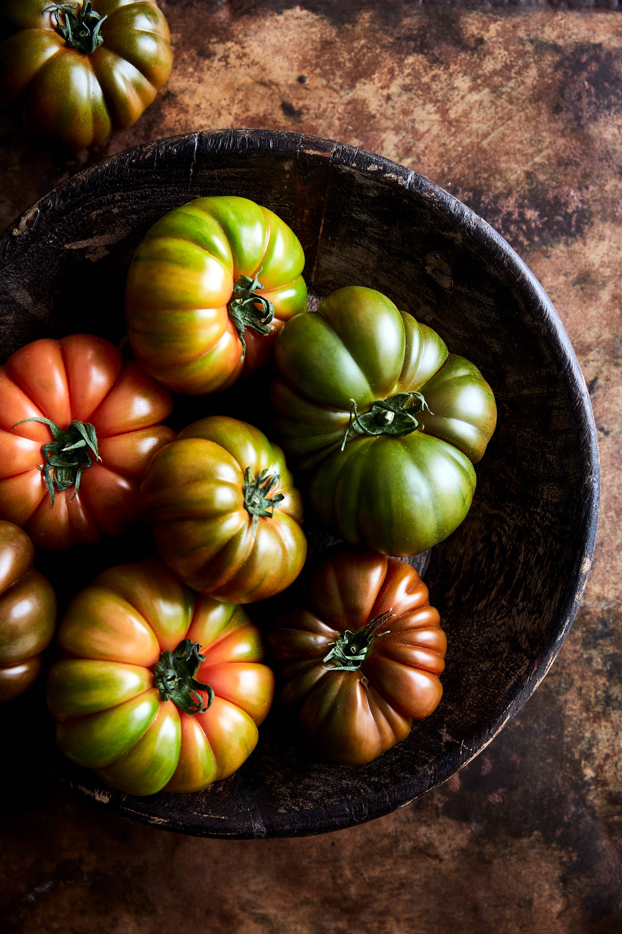 Close-up of heirloom tomatoes in a rustic wooden bowl, showcasing their vibrant colors and unique shapes against a brown background.