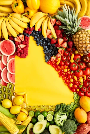 Overhead shot of assorted fresh fruits and vegetables arranged around a bright yellow backdrop, showcasing a colorful variety of produce.