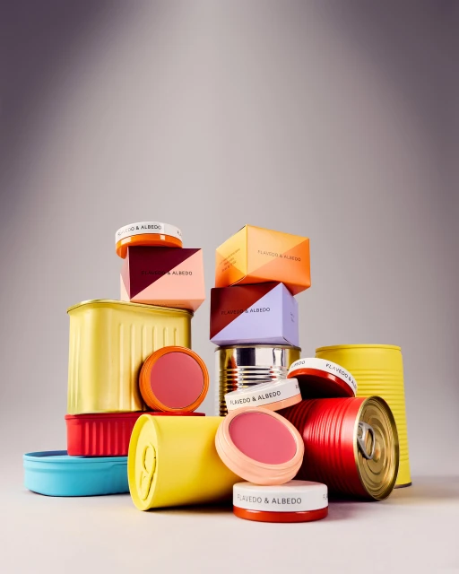 Still life arrangement of stacked colorful tin cans and cosmetic containers in a studio setting under even, soft lighting.