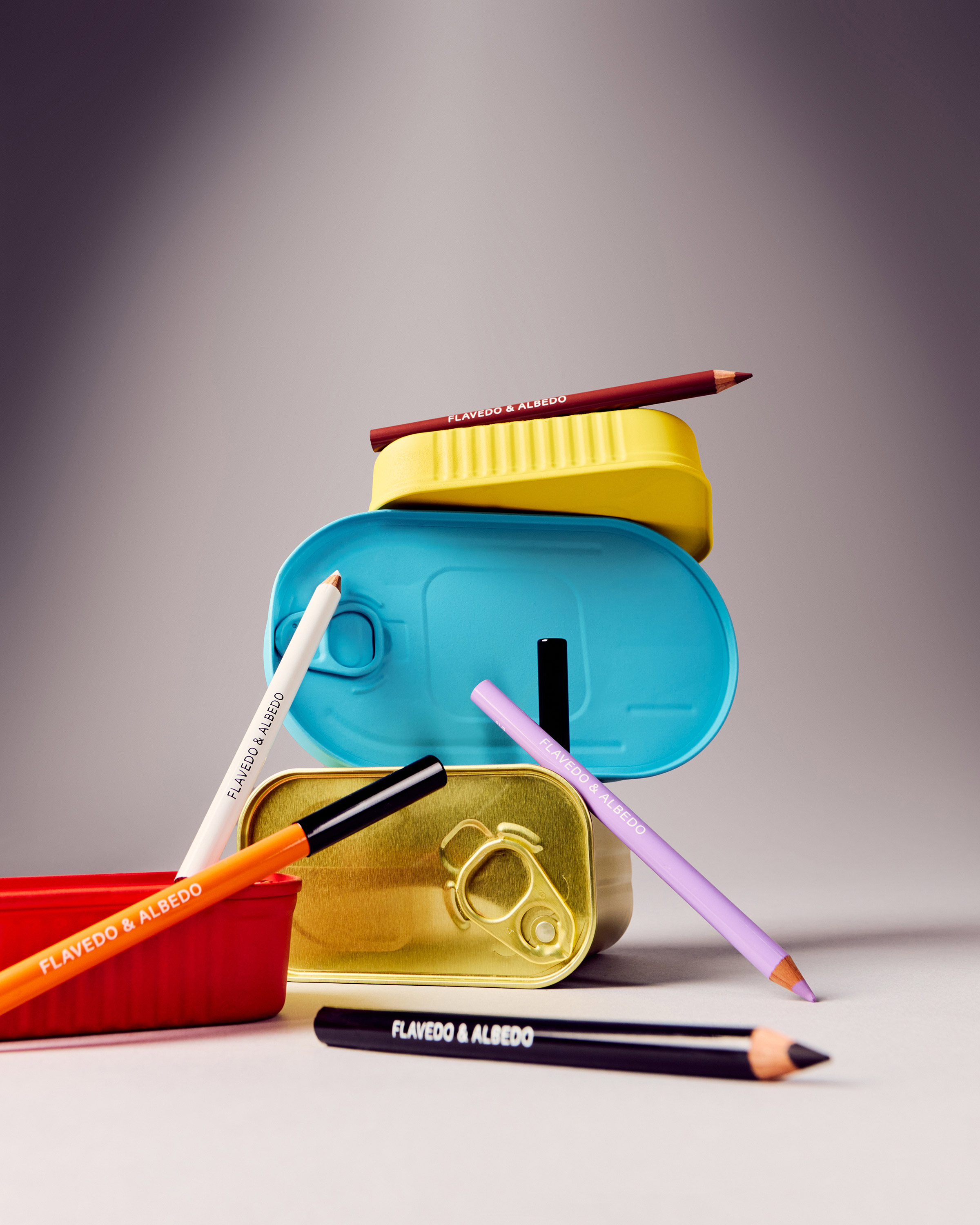 Still life studio shot of stacked colorful tuna cans with makeup pencils from Flavedo & Albedo, creating a visually striking composition.