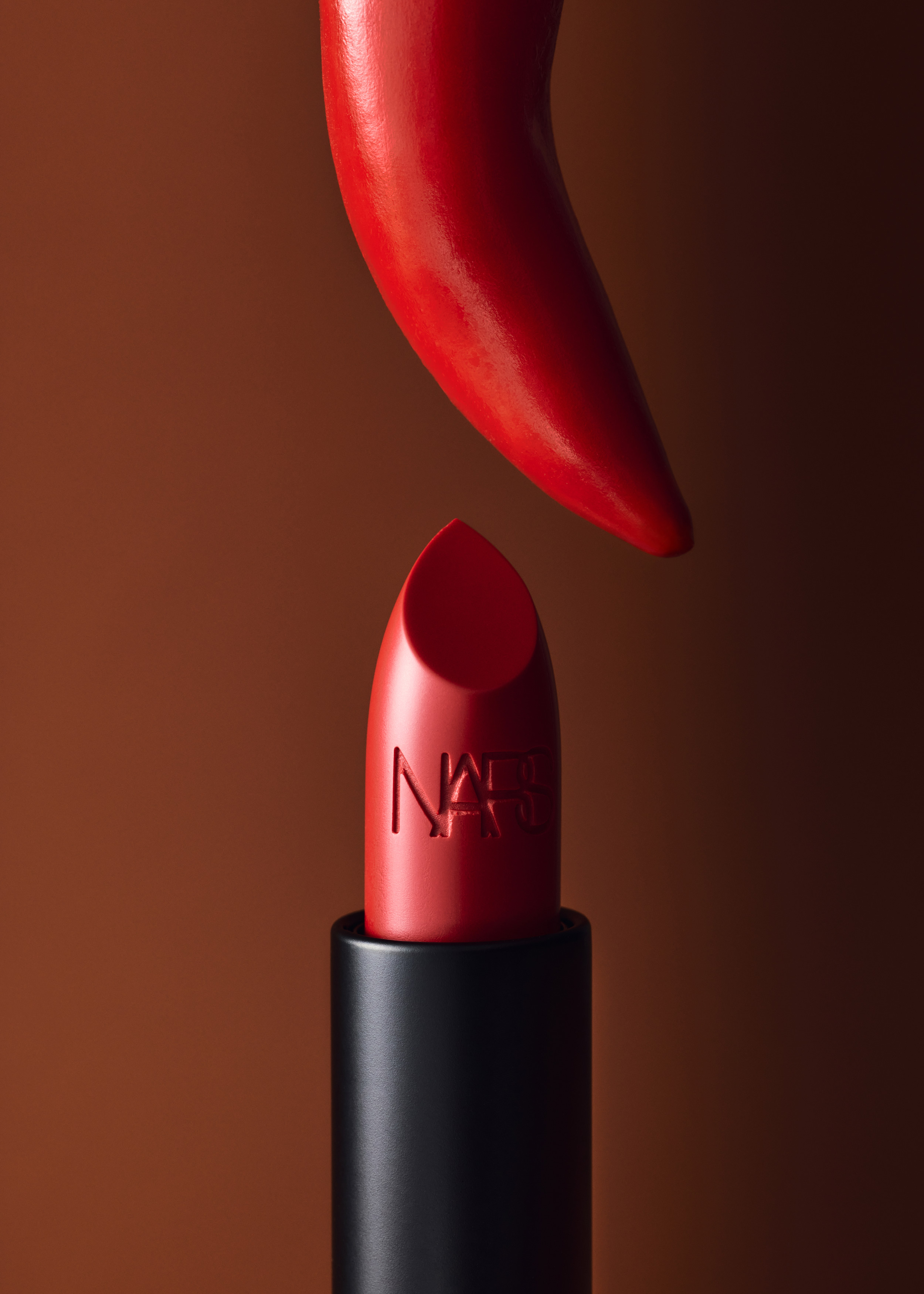 Close-up studio shot of red NARS lipstick with its cap removed, set against a warm brown backdrop.