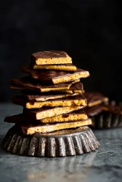 A towering stack of chocolate honeycomb pieces resting on an ornate metal plate against a moody dark background.