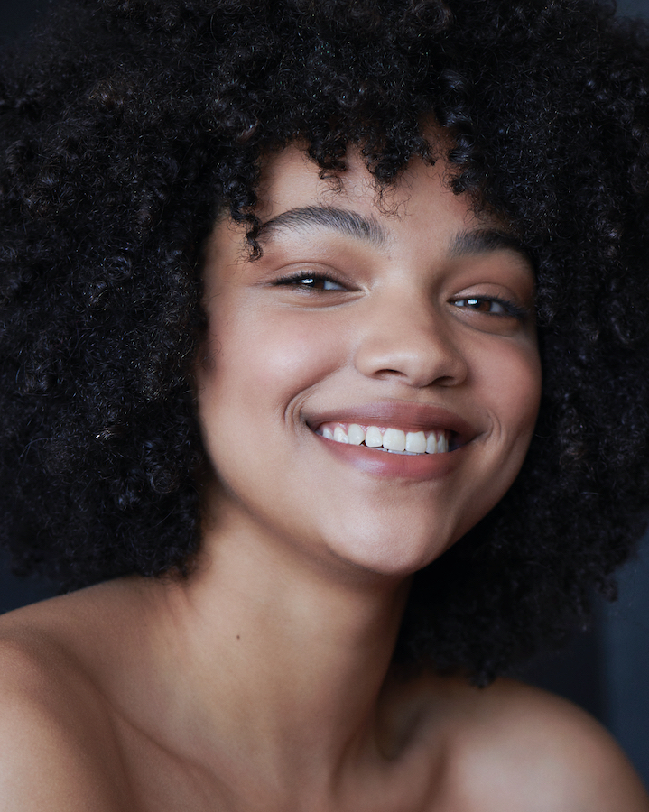 Close-up portrait of a smiling African-American woman with curly black hair, highlighting her joyful expression and clear skin.