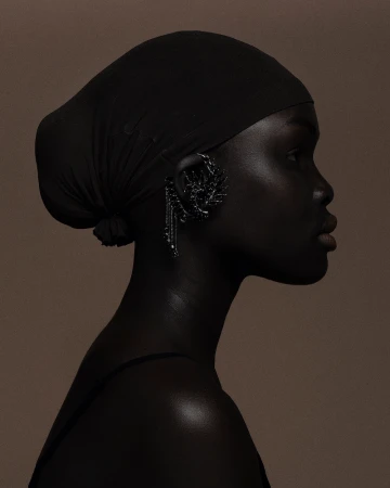 Profile portrait of a dark-skinned woman wearing a headscarf and ornate earring, set against a neutral-toned background.