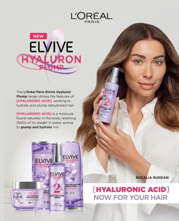 Woman with long hair holds Elvive Hyaluron Plump hair product in front of additional hair products. L'Oréal Paris branding is visible.