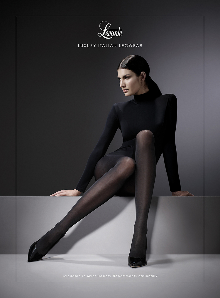 Elegant woman in black tights poses gracefully against a dark background in a fashion advertisement, showcasing luxury Italian legwear.