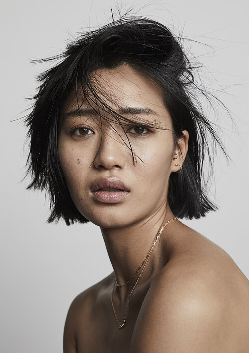Close-up portrait of an Asian woman with dark hair and a gold necklace against a neutral backdrop. Beauty, fashion, and portrait photography.