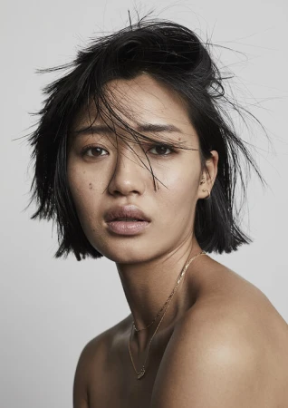 Close-up portrait of a woman with short dark hair and natural makeup against a plain light grey background