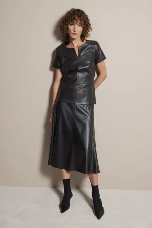 Full-length studio shot of a woman in a black faux-leather top and skirt with matching sheer socks and black pointed-toe heels.