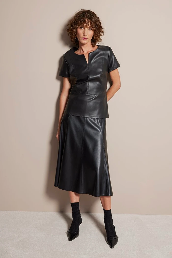 Woman in black leather top and midi skirt posing against a neutral grey studio backdrop in Melbourne.