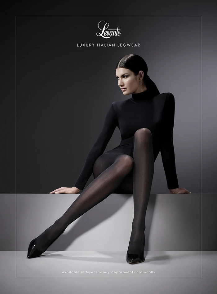 Model in black turtleneck and tights seated on a grey studio block by Marija Ivkovic