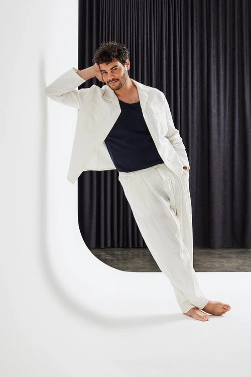 Man in white suit and dark t-shirt leaning against a white curved studio wall by Marija Ivkovic