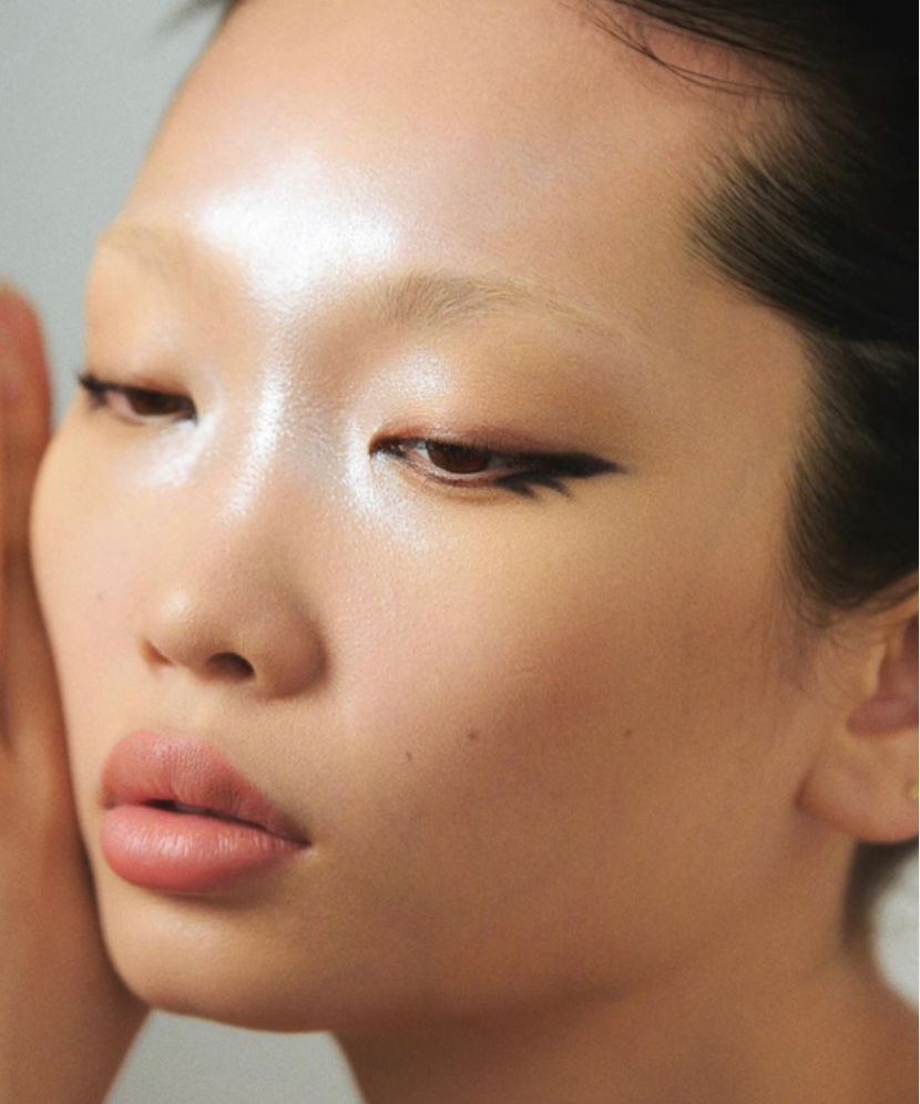 Close-up portrait of an Asian adult female with light skin, wearing winged eyeliner and light pink lipstick, set against a plain background.
