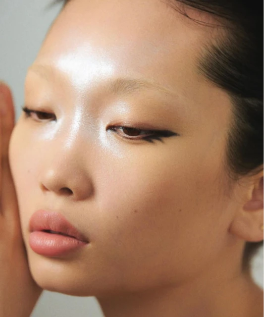 Close-up portrait of an Asian adult female with light skin, wearing winged eyeliner and light pink lipstick, set against a plain background.