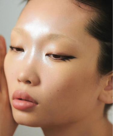 Close-up portrait of an Asian adult female with light skin, wearing winged eyeliner and light pink lipstick, set against a plain background.