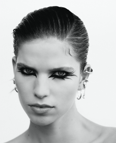 Close-up portrait of a woman with dramatic black graphic eyeliner and stacked silver ear cuffs against a white background