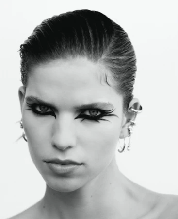 Close-up portrait of a woman with dramatic black graphic eyeliner and stacked silver ear cuffs against a white background