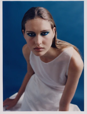 Woman in white dress with dramatic blue eye makeup posing against a solid blue studio backdrop