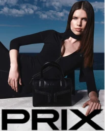 Woman in black top resting near a black handbag outdoors with ocean view and bold Prix lettering