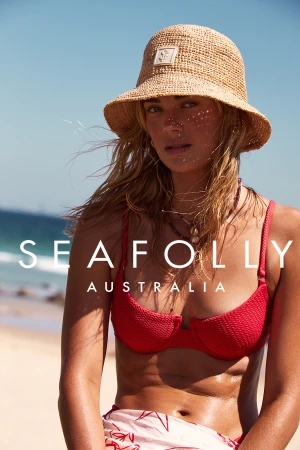 Woman wearing a straw bucket hat and red bikini top on a sandy beach under bright sunlight by photographer Lauren Schulz
