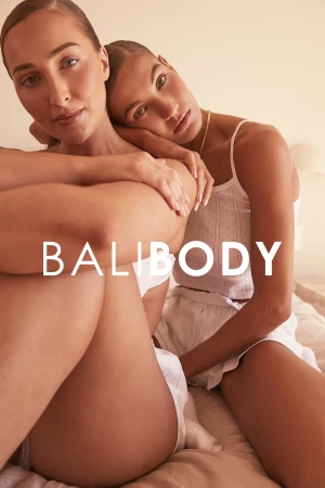 Two adult women pose closely indoors wearing loungewear in a medium shot, with 'Bali Body' text overlayed in white, creating a beauty or fashion advertisement.