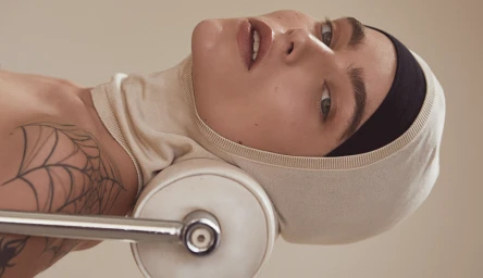 Close-up portrait of a woman wearing a cream hood and black headband resting against a white cylindrical support in Melbourne by Lauren Schulz