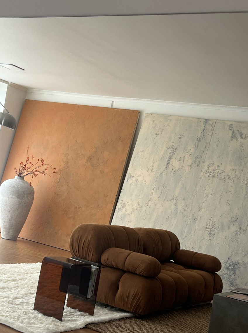 Brown Togo sofa with a vase of flowers against a backdrop of painted panels in a brightly lit interior space, creating a modern living room aesthetic.