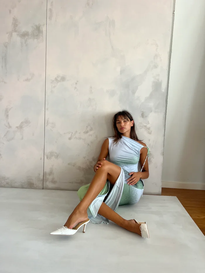 Woman in pale blue and green dress sitting against a mottled concrete wall in Melbourne by Spectrum Haus