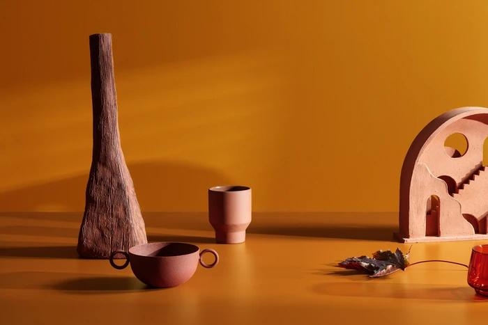Still life arrangement with textured ceramic vessels and a sculptural arch object on a warm yellow surface.