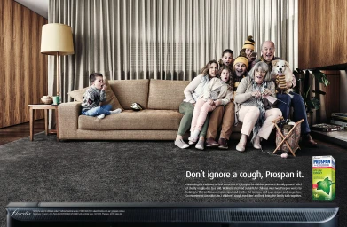 Large family and dog gathered on a brown sofa in a living room while a young boy yawns on the other end.