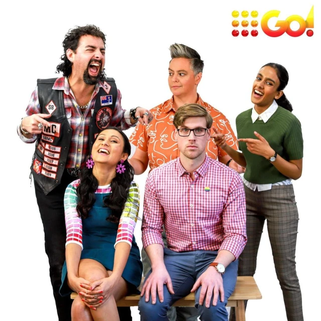 Group shot of five people in unique outfits posing on a white background. The people are on a wooden bench and smiling.