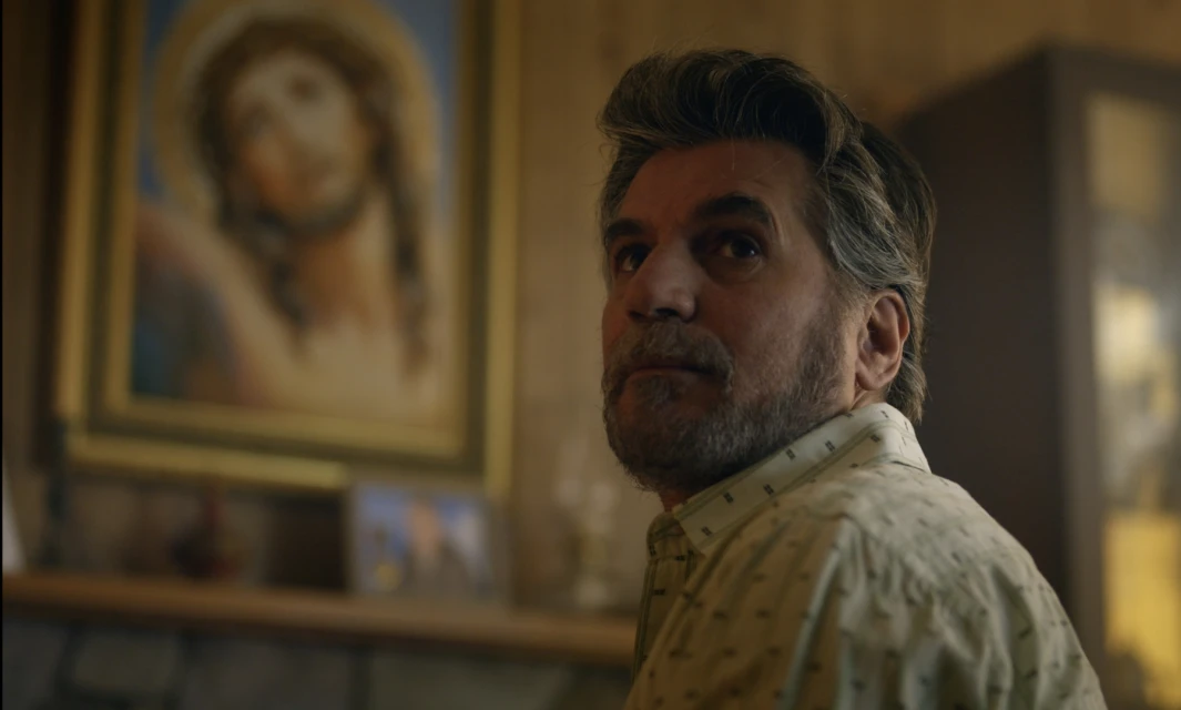 Man looks upward in an indoor setting with a painting of Jesus Christ visible in the background, in a medium shot.