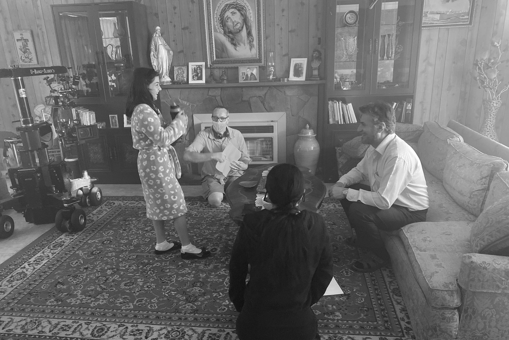 Behind the scenes on a film set with director, actors, and camera equipment in a home interior, captured in black and white.