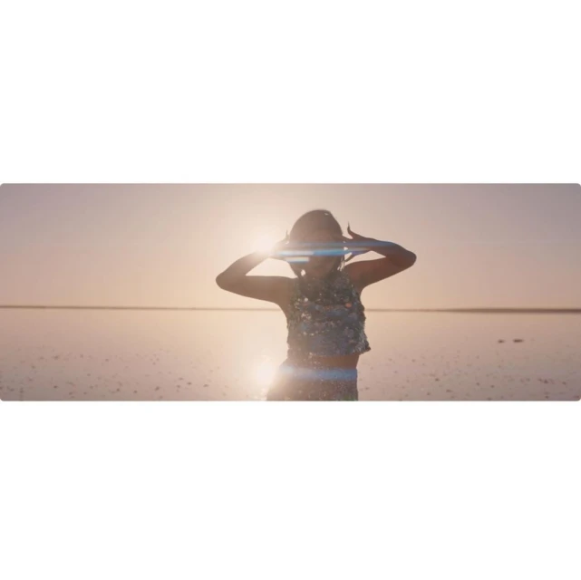 Woman in sequin top stands in the shallow water of a salt flat at sunset, her hands above her head in celebration.