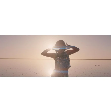 Woman in sequin top stands in the shallow water of a salt flat at sunset, her hands above her head in celebration.